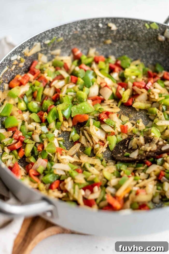 Diced bell peppers, onions, and minced garlic simmering in a large skillet, creating a fragrant base for the black beans and rice.