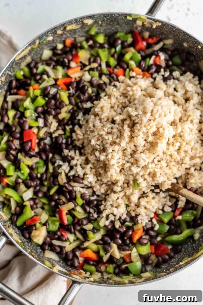 A large scoop of fluffy brown rice being carefully added to a simmering skillet of flavorful black beans and sautéed vegetables, ready to be combined.