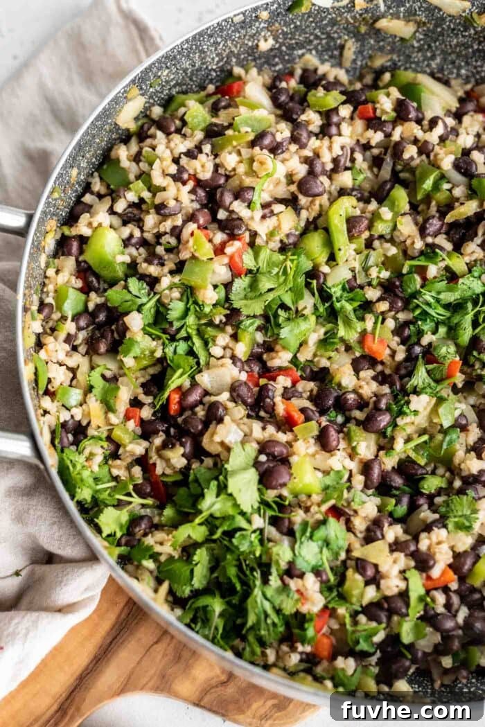 A close-up view of the finished vegan black beans and rice, brimming with colorful vegetables and fresh cilantro, steaming gently in a large skillet.