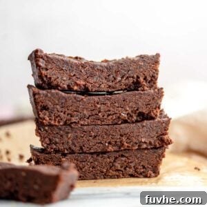 Effortless Chocolate Protein Treats 9 Stack of 4 chocolate protein bars on parchment paper on a marble cutting board.