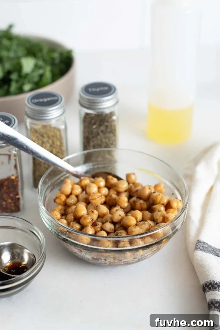 A small bowl containing chickpeas mixed with balsamic vinegar and various dried herbs, ready for marinating, with a spoon resting in the bowl.