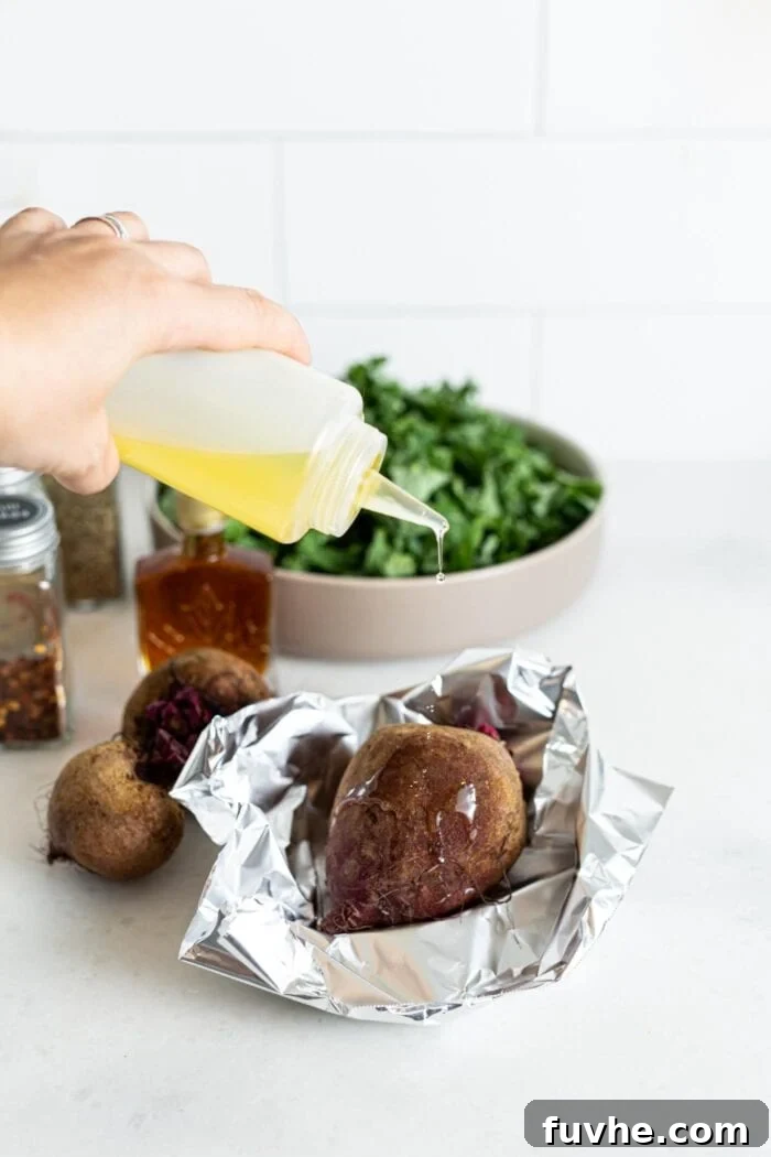 A single beet, lightly drizzled with olive oil, being wrapped in aluminum foil on a baking sheet, preparing it for roasting.