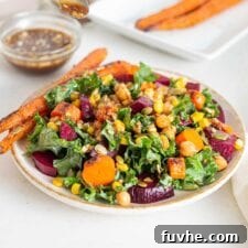 A bowl of roasted beet kale salad with corn, carrots, chickpeas, and pumpkin seeds.