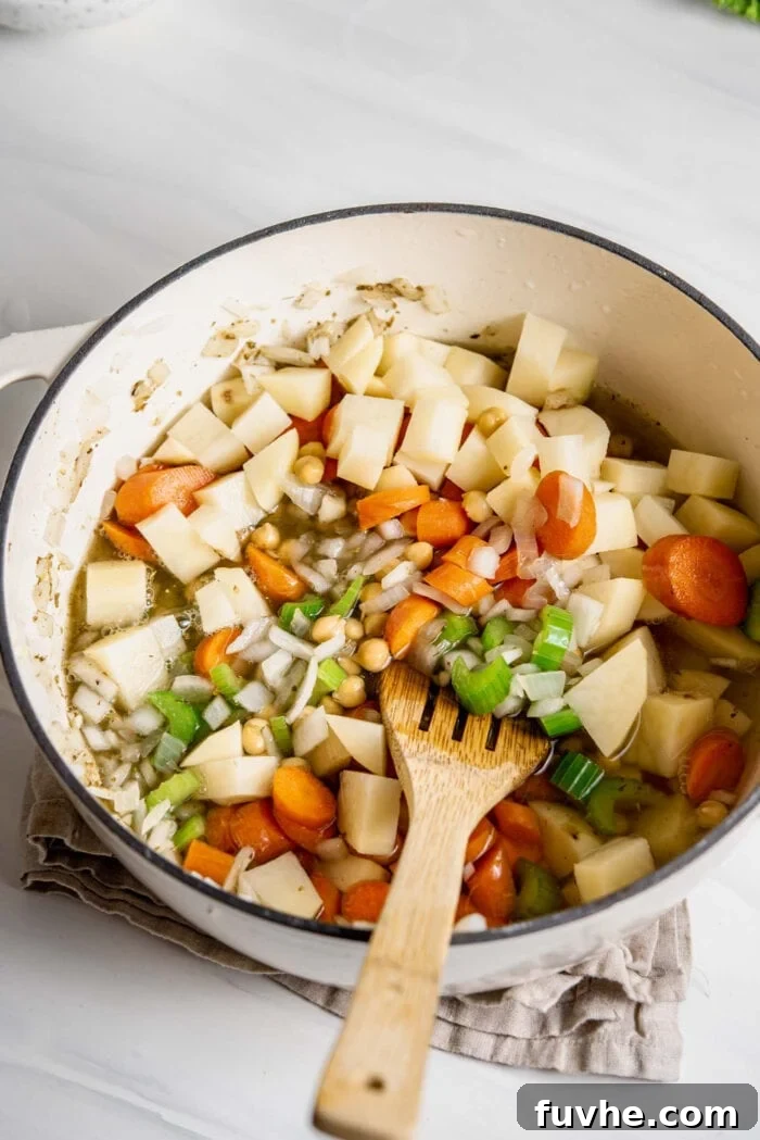 Potato, celery, carrots and chickpeas cooking in broth in a large soup pot.