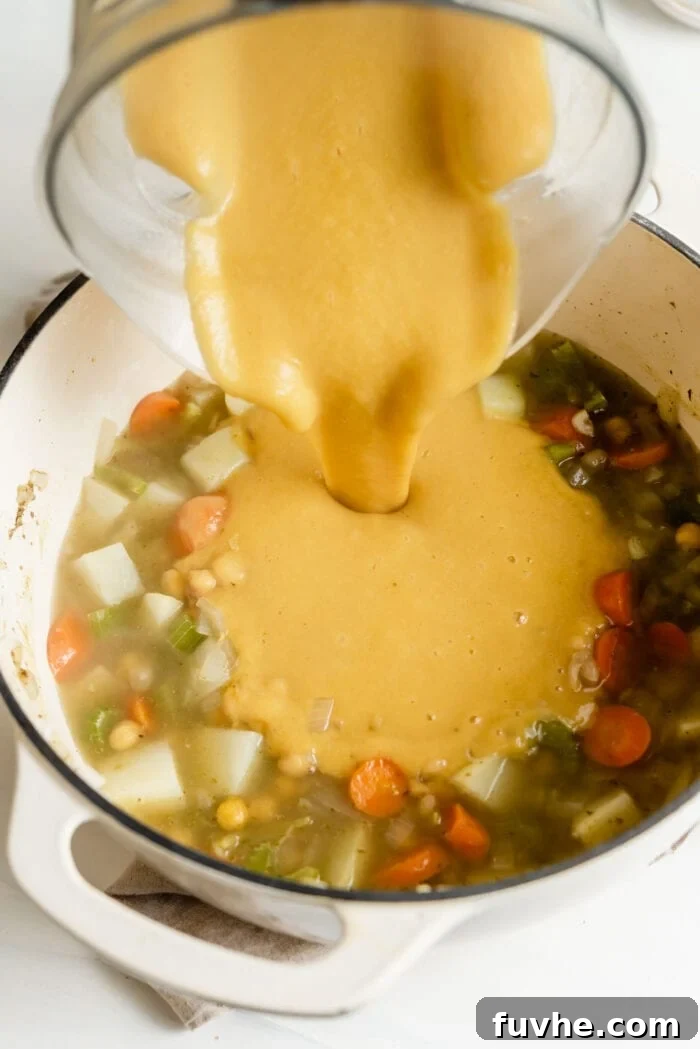 Pouring pureed chickpea soup back into a pot of chunky soup.