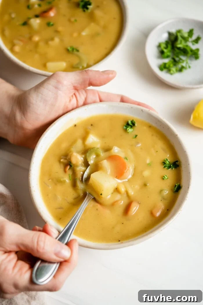 Hand using a spoon to take a spoonful of vegetable chowder out of a bowl.