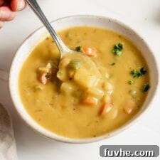 Hand using a spoon to take a spoonful of vegan chickpea soup from a bowl.