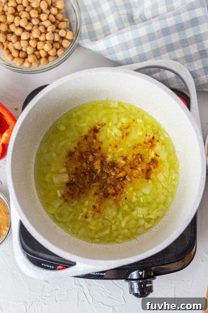 A close-up shot of sautéed celery, onion, and various spices being stirred in a large soup pot, releasing their aromatic fragrance.