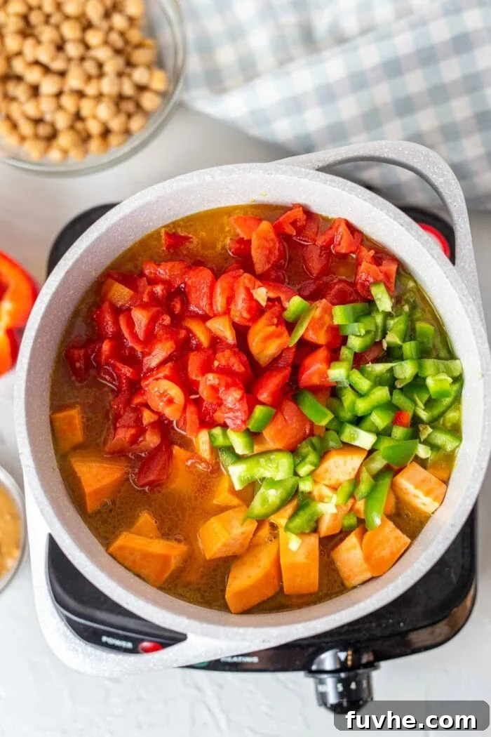 A large pot filled with a colorful medley of sweet potato chunks, diced tomatoes, and bell peppers, simmering gently, creating a rich broth.