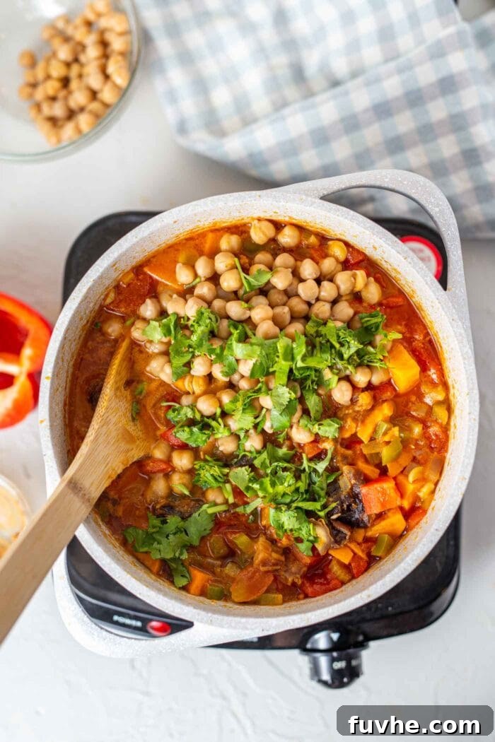A close-up of a large pot of sweet potato peanut stew with vibrant green cilantro being stirred in, indicating the final stage of preparation.