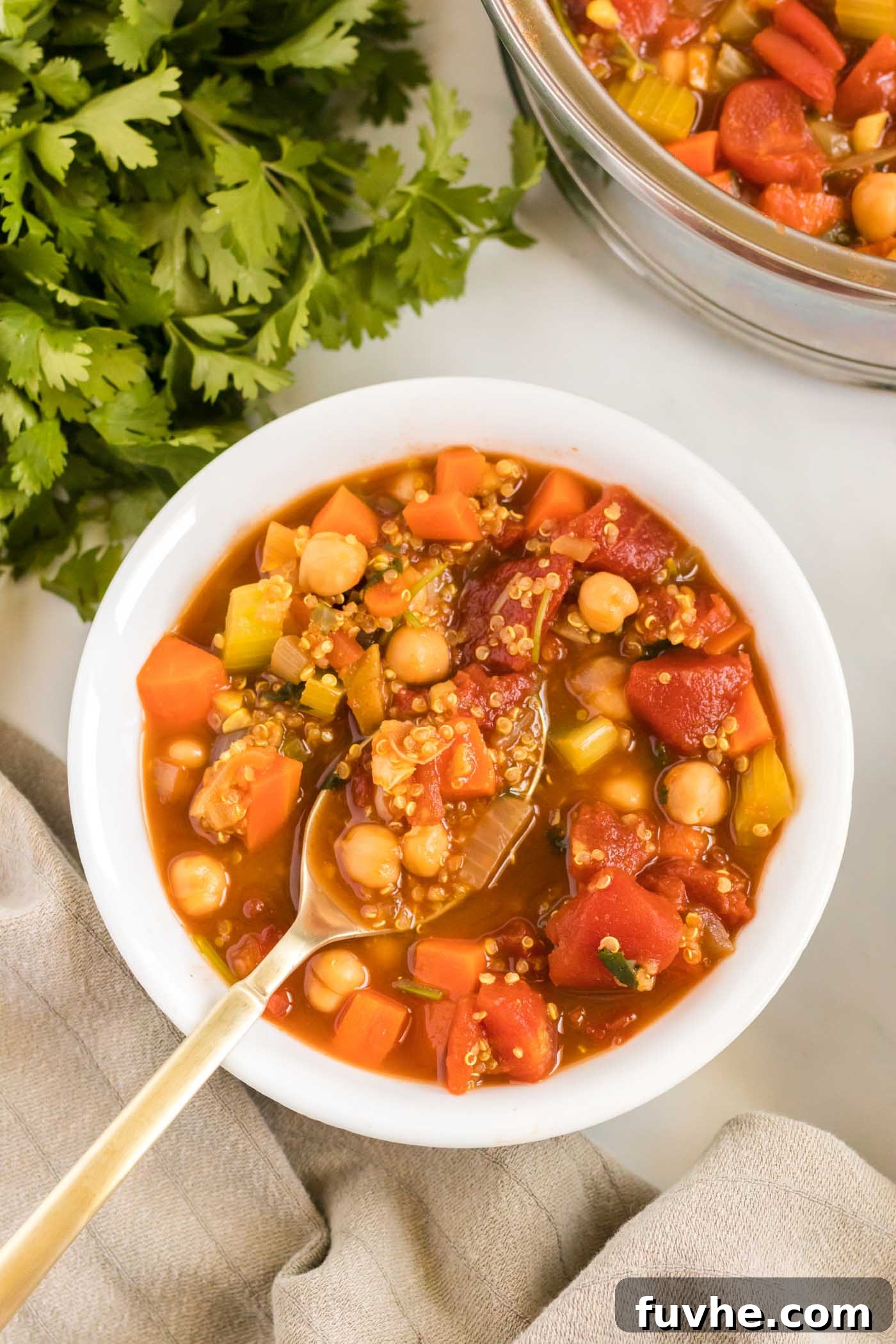 Overhead view of a steaming bowl of vegan chickpea quinoa stew with a spoon, garnished with fresh herbs.