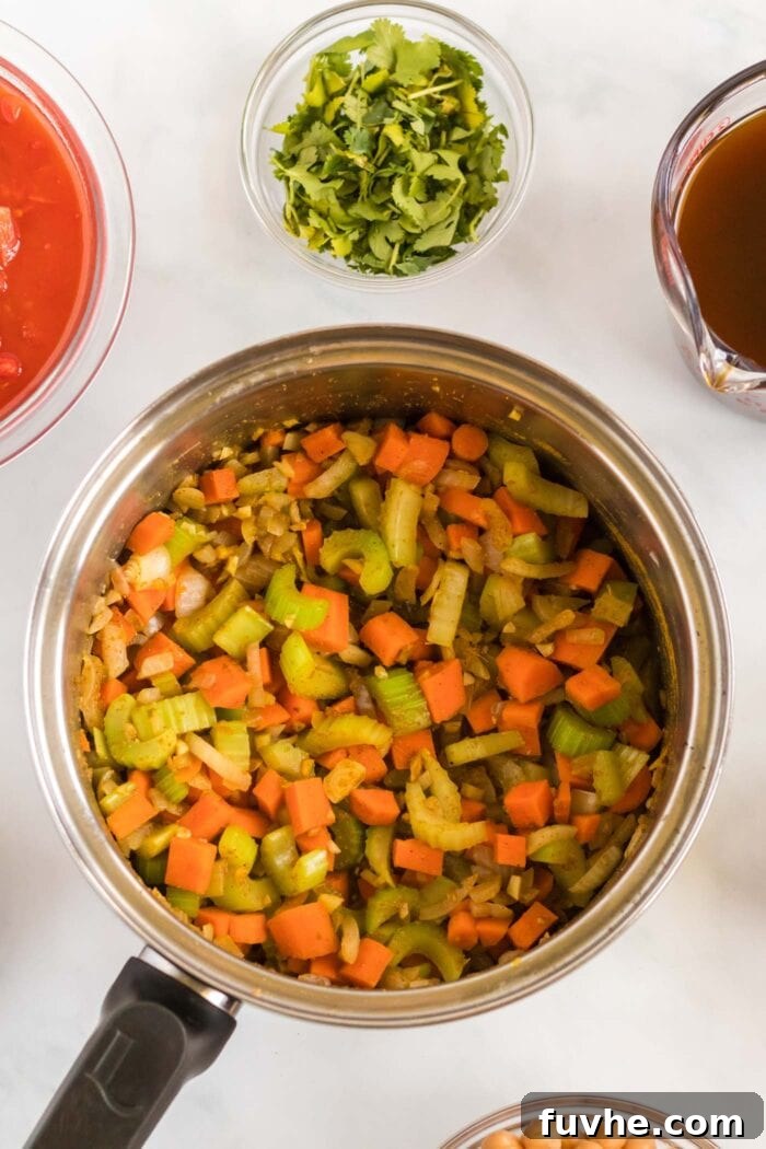 A vibrant mix of cooked diced celery, carrot, and onion in a soup pot, now beautifully infused with fragrant bloomed spices, ready for the next liquid ingredients.