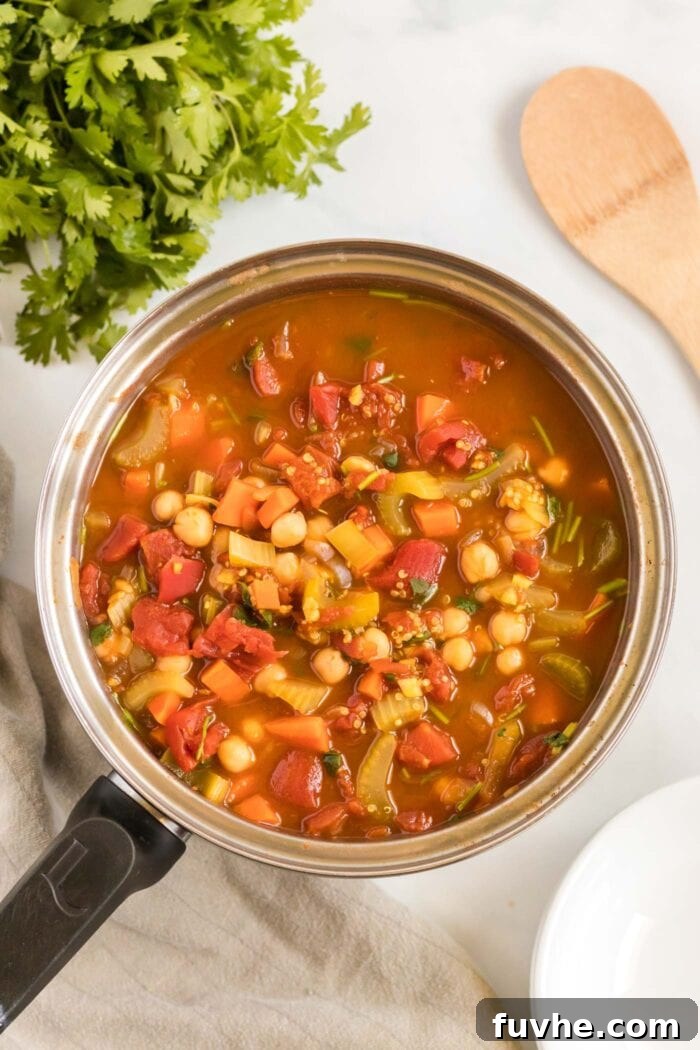 A vibrant, finished tomato stew with tender chickpeas and fluffy quinoa cooking gently in a soup pot, garnished with fresh herbs, ready to be served and enjoyed.