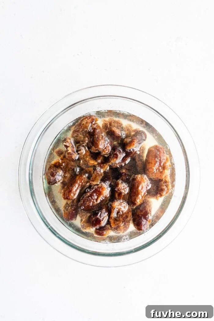 Effortless Vegan Peanut Butter Blondies 4 Pitted dates soaking in hot water in a glass bowl, preparing them for the creamy date caramel frosting.
