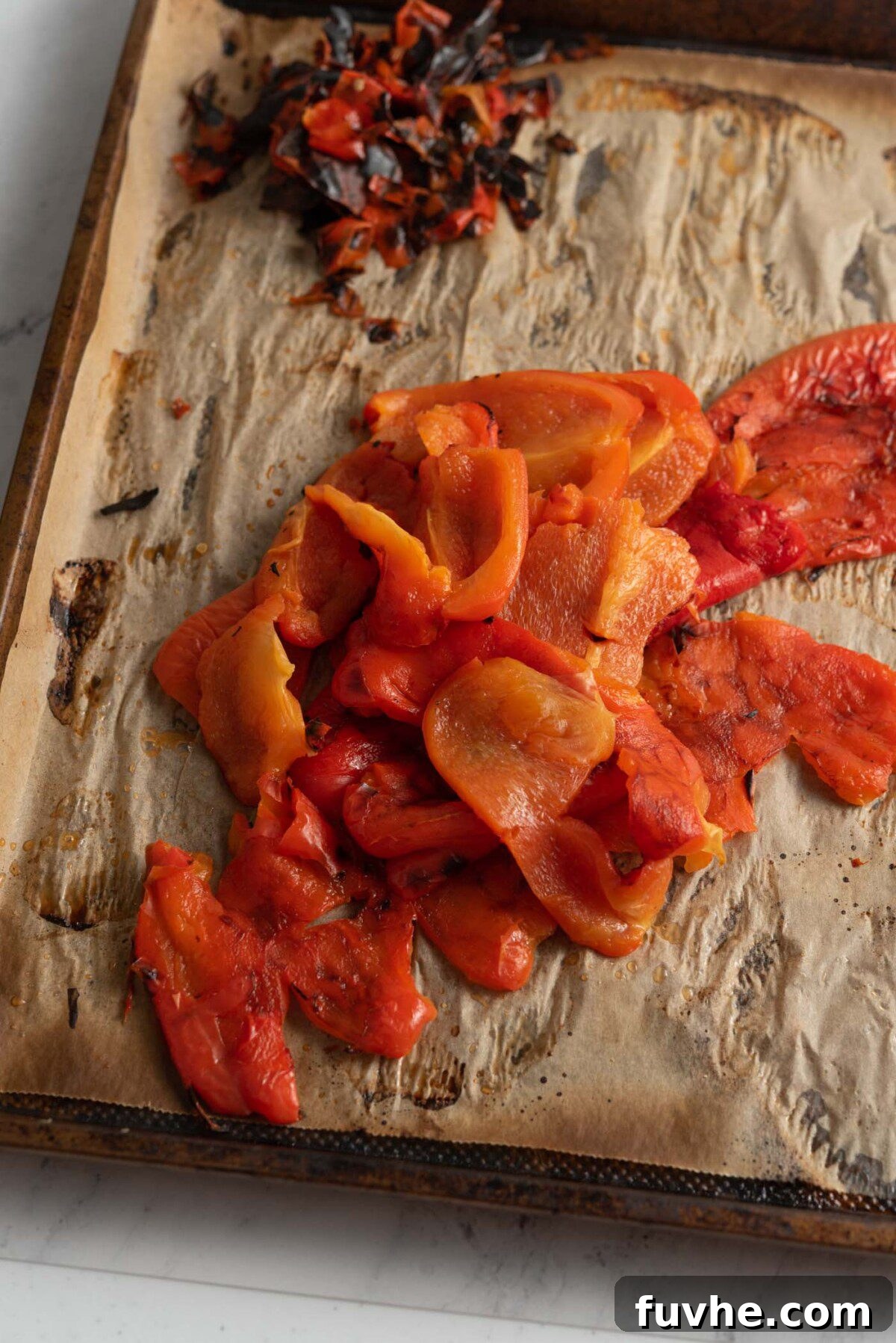 A pile of perfectly peeled roasted red peppers, showcasing their tender, sweet flesh after careful preparation on a baking tray.