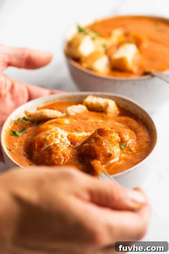 A close-up shot of a spoon laden with creamy roasted red pepper tomato soup, about to be savored, highlighting the soup's rich texture and inviting warmth.