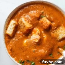 Overhead view of a bowl of red pepper tomato soup topped with cubes of toasted bread.