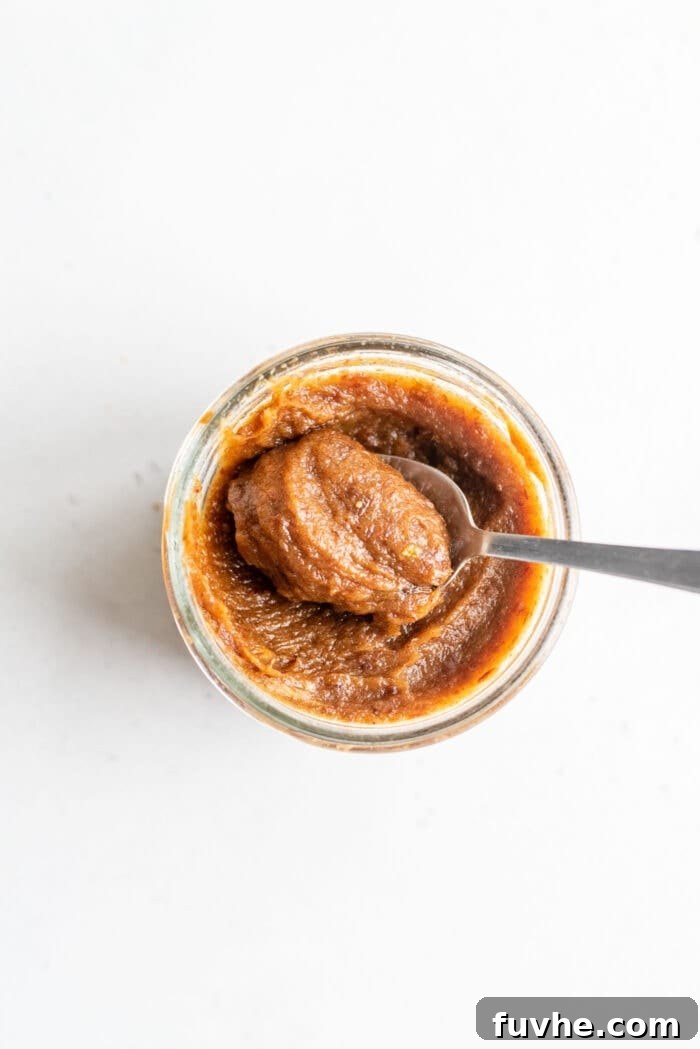 Sweet Swaps from Nature 10 A spoon scooping date paste out of a small glass jar on a white background.