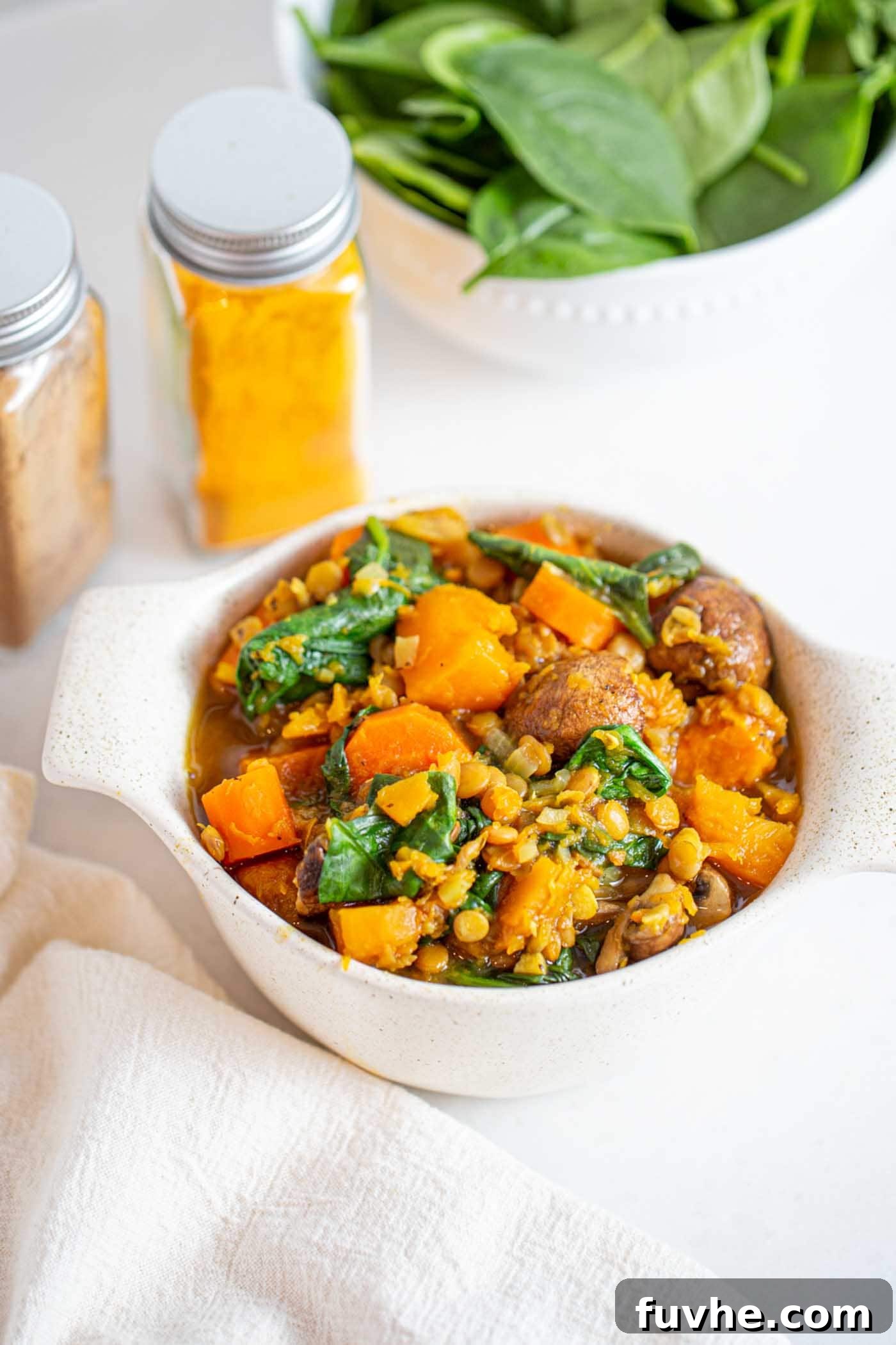 Golden Squash Lentil Pot 2 A vibrant bowl of butternut squash and lentil stew, garnished with fresh herbs and a swirl of creamy coconut milk, sits invitingly on a rustic wooden table.