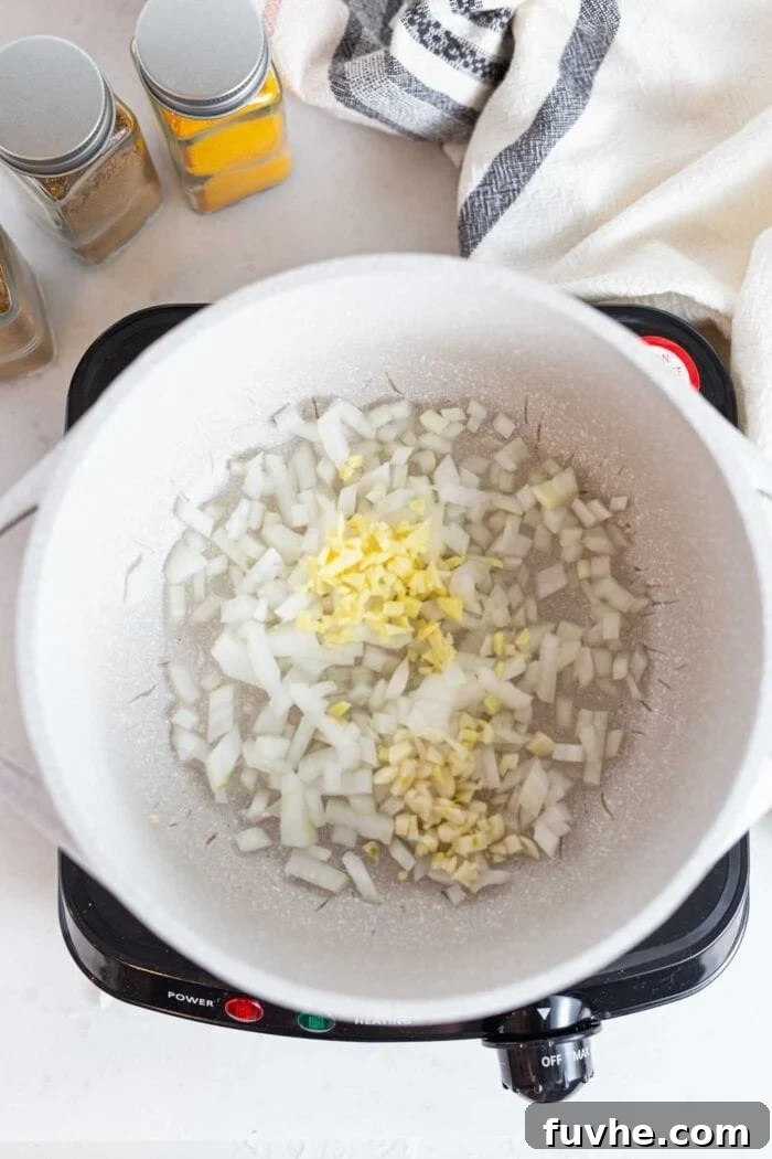 Golden Squash Lentil Pot 4 Onions, garlic, and ginger sizzling and sautéing in a large pot on the stovetop, releasing their aromatic flavors.