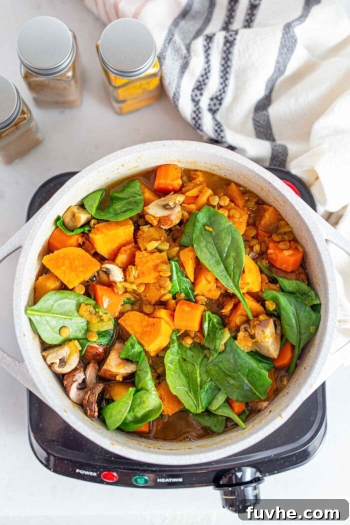 Golden Squash Lentil Pot 7 A vibrant, bubbling pot of spinach, mushroom, and squash stew cooking gently on the stovetop, steam rising from the nourishing meal.