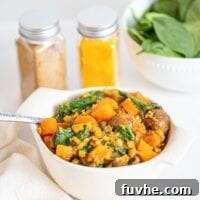 A bowl of butternut squash and lentil stew, beautifully presented with vibrant mushrooms and fresh spinach.
