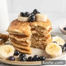 Close up of a stack of pancakes that have been sliced to show the texture inside. The pancakes are topped with blueberries and banana.