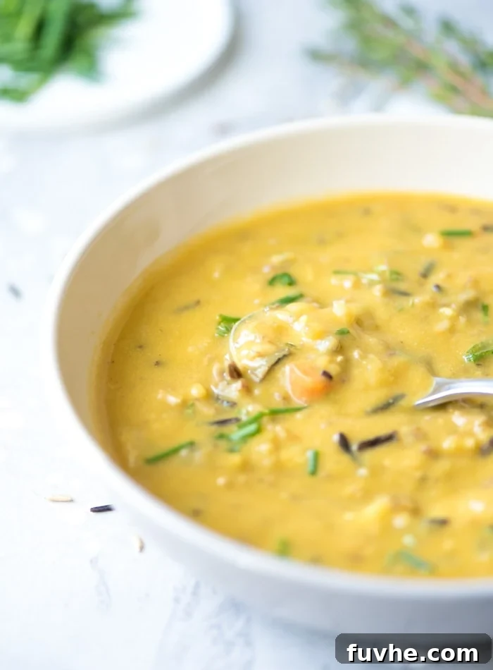 Bowl of creamy cauliflower wild rice soup topped with chopped chives. Spoon rests in bowl.