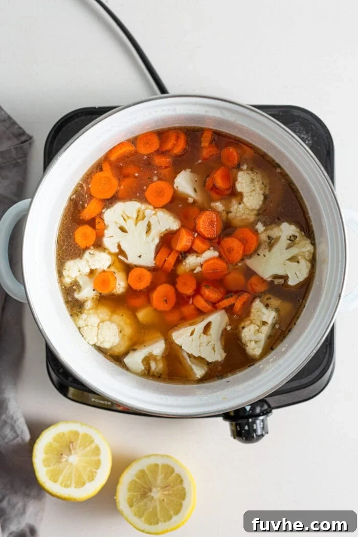 Carrots and cauliflower cooking in broth in a soup pot.