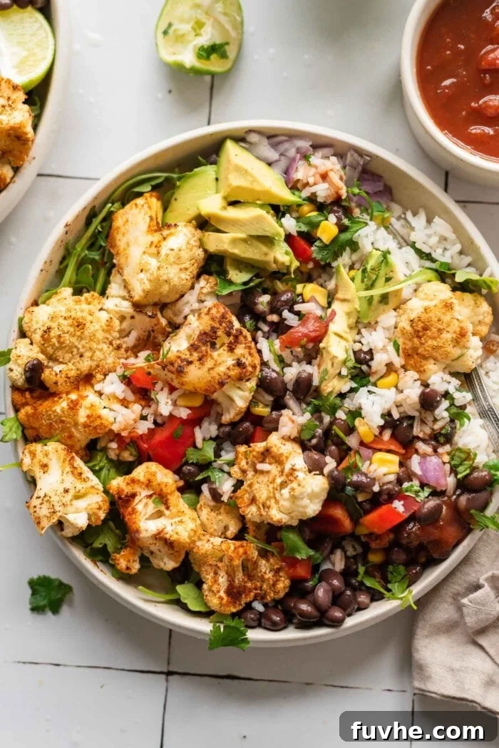 Overhead view of a vibrant burrito bowl with fluffy rice, perfectly roasted cauliflower, creamy avocado slices, and seasoned black beans, showcasing a delicious vegan meal option.
