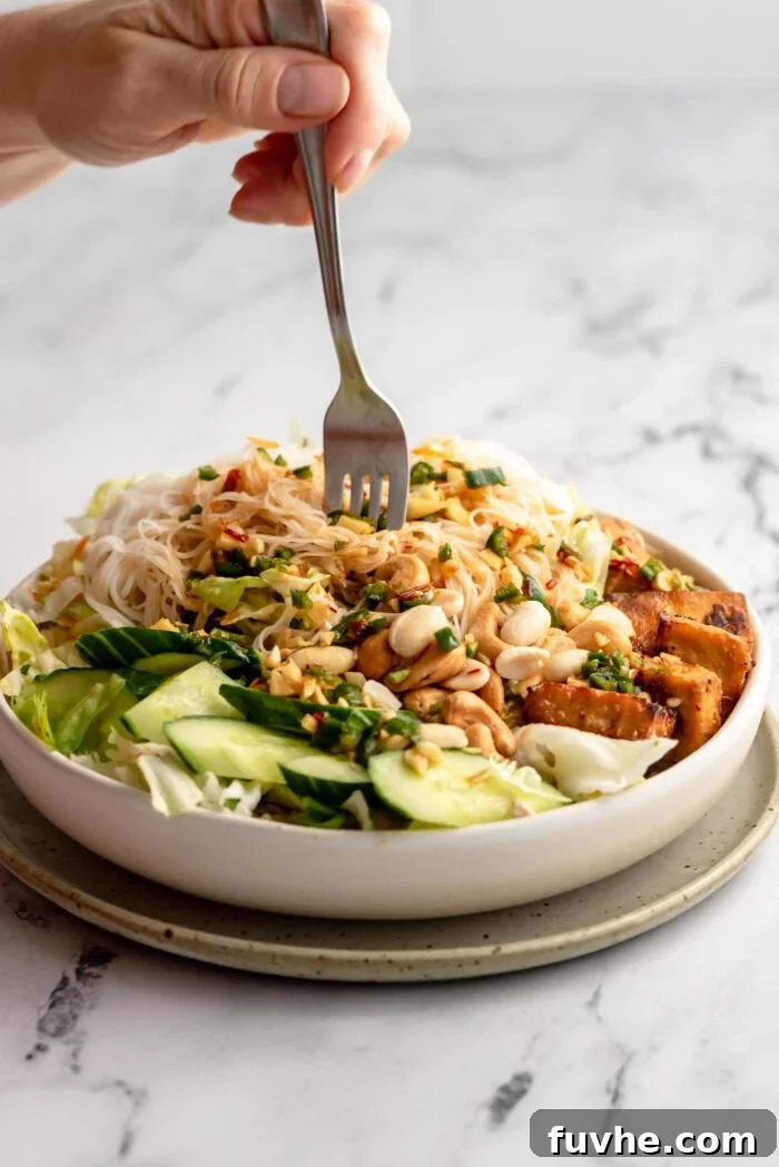 A hand gracefully using a fork to enjoy a vibrant Tofu Vermicelli Salad, brimming with fresh ingredients and flavorful tofu pieces.
