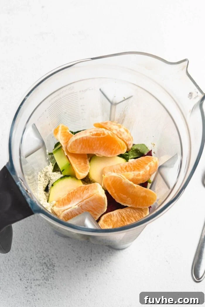 A dynamic shot capturing an orange, fresh spinach, a slice of zucchini, and a scoop of protein powder poised within a blender, ready to create a healthy and vibrant smoothie.