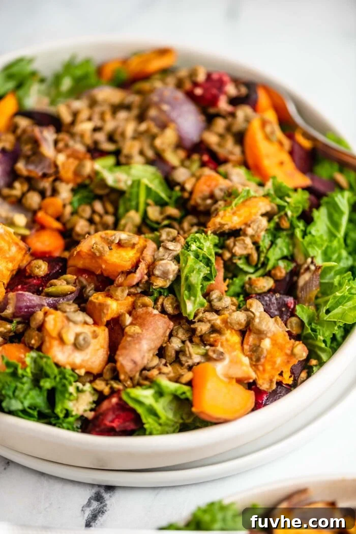 A close-up view of a vibrant bowl featuring a healthy kale sweet potato salad, generously mixed with protein-rich lentils, colorful beet slices, shredded carrots, and finely chopped red onion.