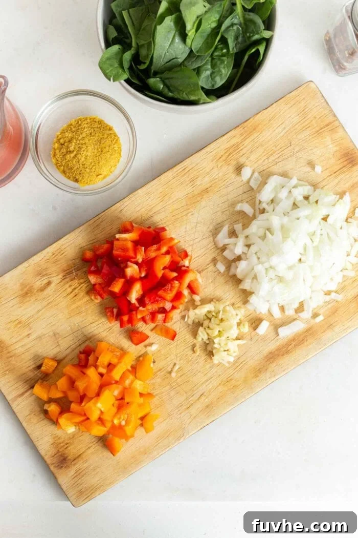 A vibrant display of freshly chopped bell peppers, onions, and garlic on a cutting board, elegantly positioned beside a bowl brimming with fresh spinach, showcasing essential ingredients for a healthy meal.