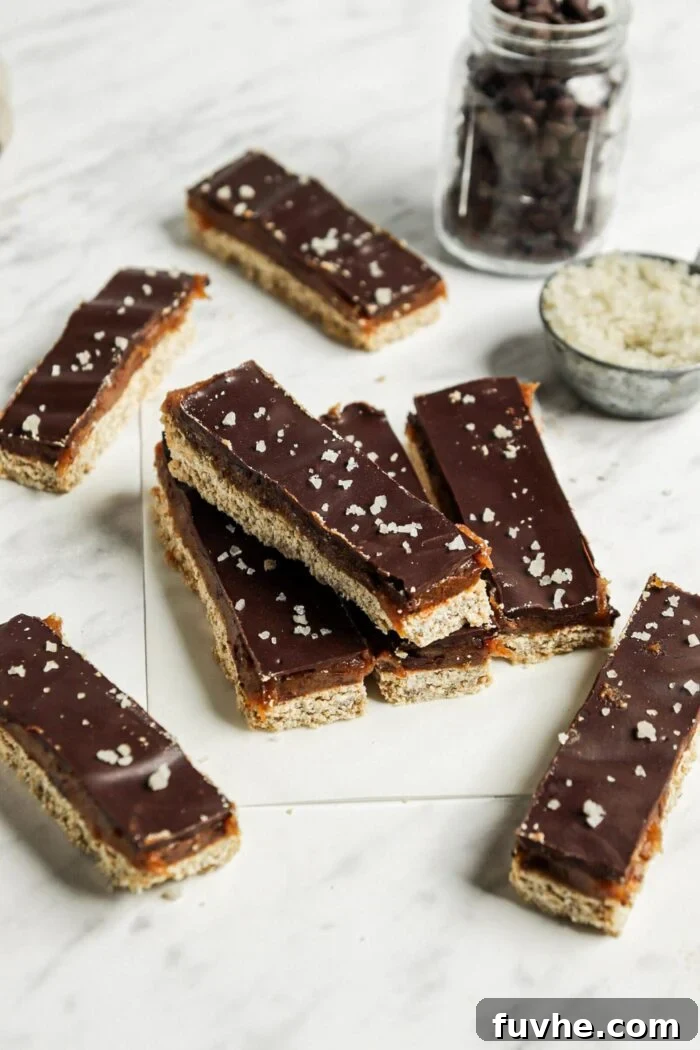 A selection of meticulously crafted homemade Twix candy bars beautifully arranged on a white marble surface, lined with crinkled parchment paper, highlighting their delicious and appealing texture.
