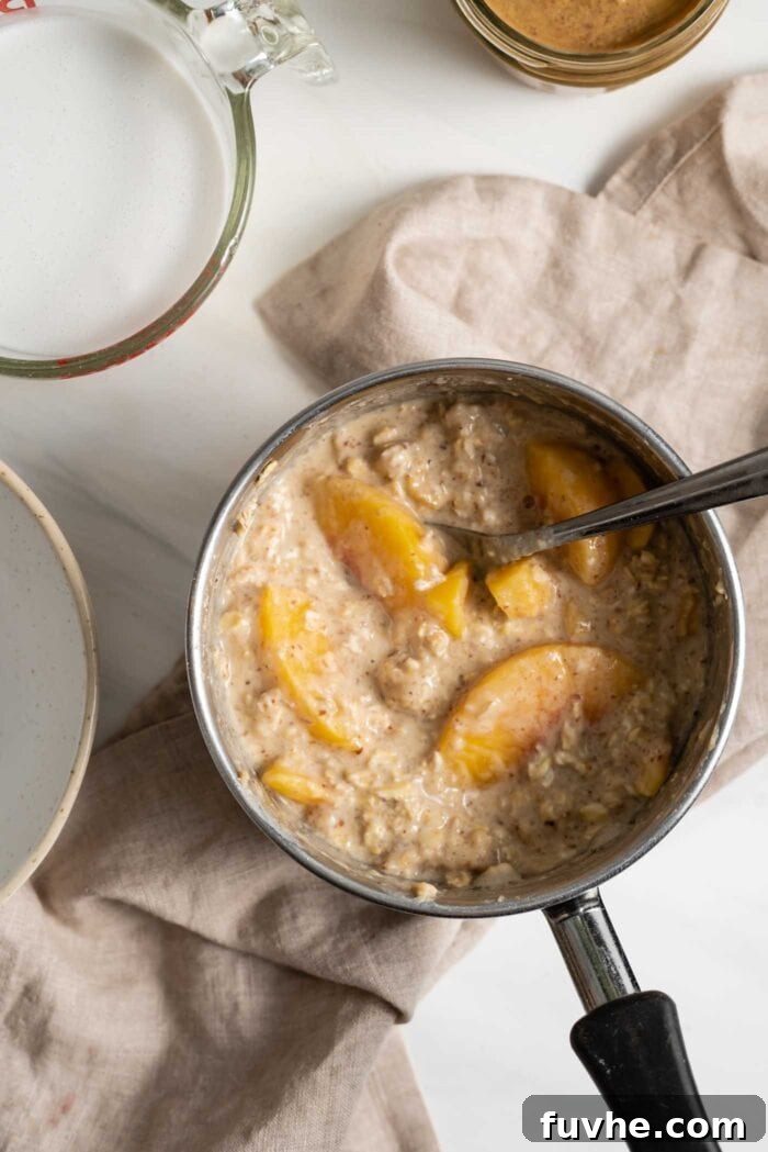 Velvety Vegan Peach Dream Bowl 4 Cooked oatmeal with peaches in a saucepan.