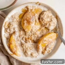 Velvety Vegan Peach Dream Bowl 6 A bowl of peaches and cream oatmeal with a spoon in it.