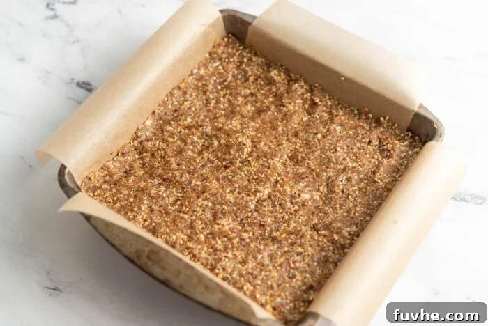 Energy bars pressed firmly into a parchment paper-lined square baking pan, ready for chilling.