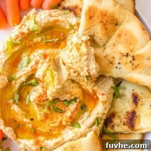 A triangle of pita being dipped into hummus that's sprinkled with parsley, paprika and drizzled with olive oil.