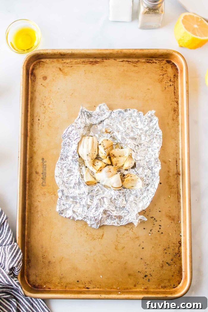 Roasted cloves of garlic in a crumbled piece of foil on a baking sheet.