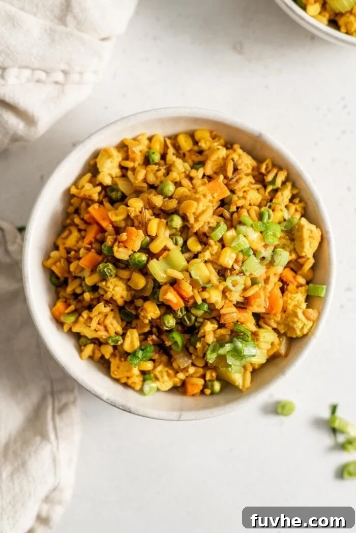A bowl of vegan fried brown rice with veggies and scrambled tofu.