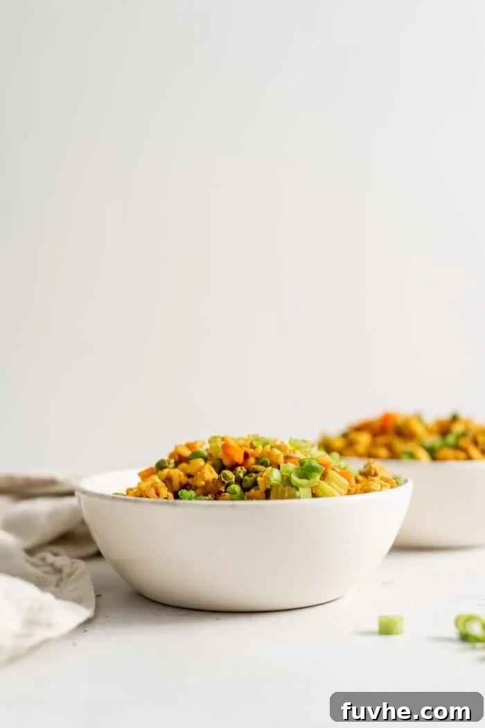 Two bowls of vegan fried brown rice with a few pieces of green onion scattered around.