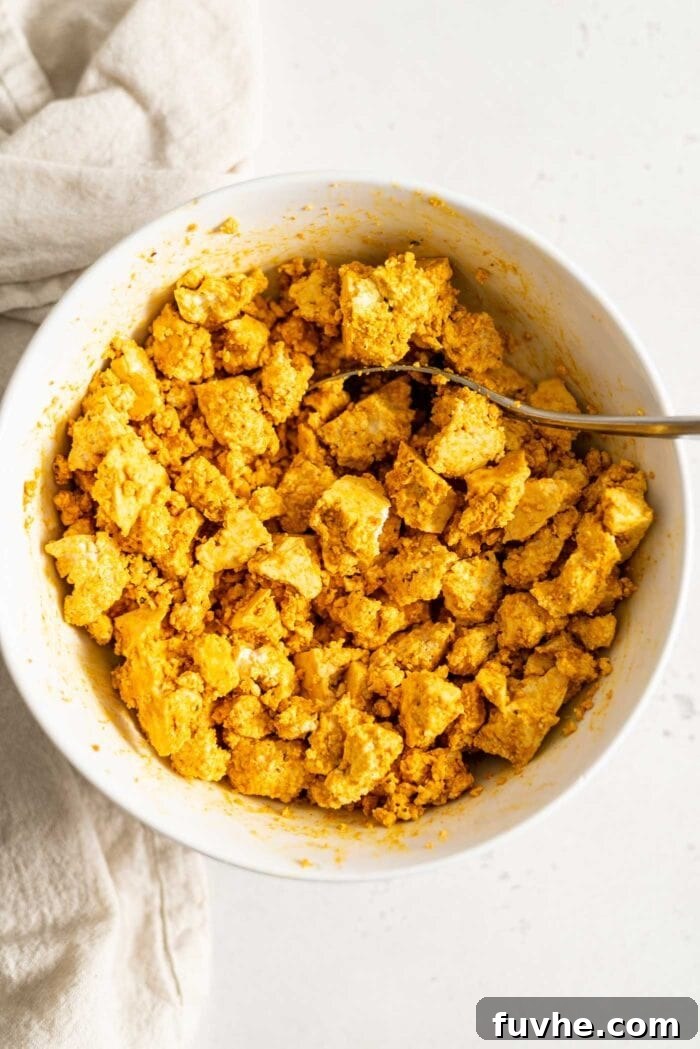 Crumbled firm tofu mixed with turmeric in a white bowl.
