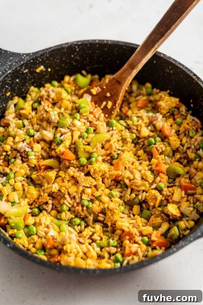 Vegan fried brown rice in a large skillet with a wooden spoon.