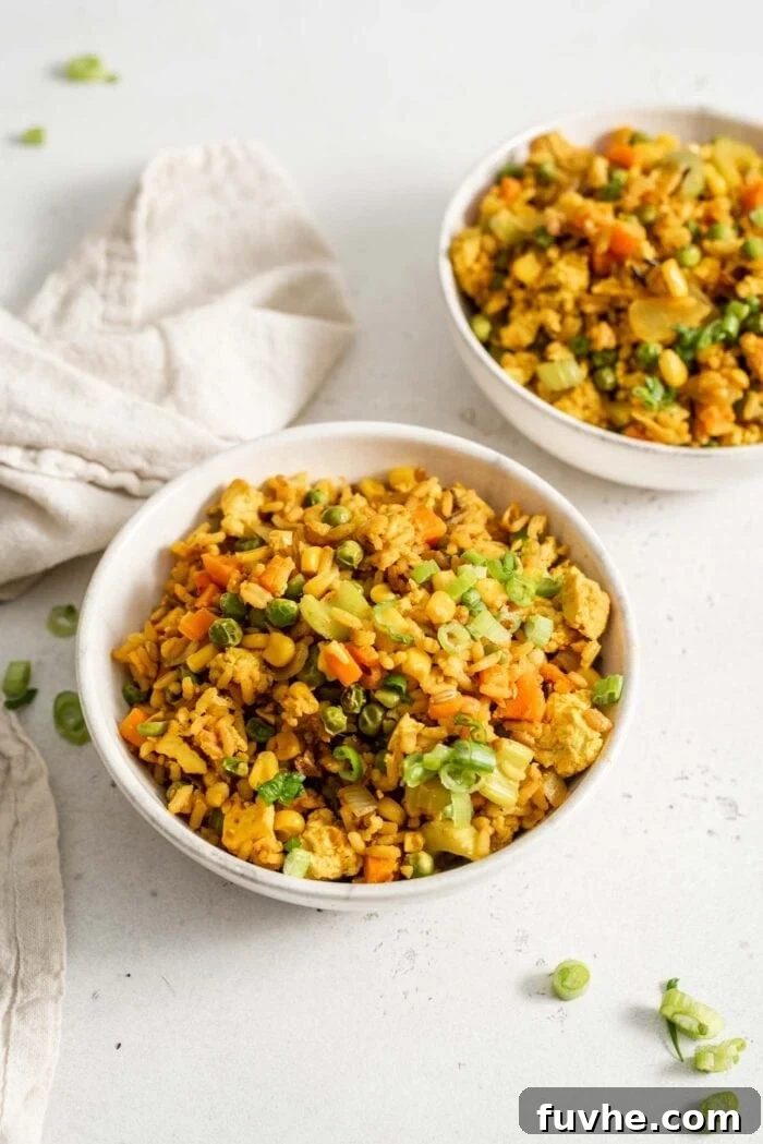 Two bowls of vegan fried brown rice sitting on a white surface.