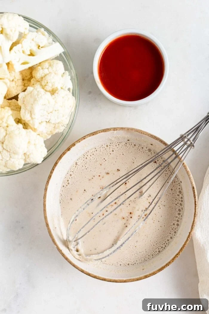 Tangy Buffalo Cauliflower Wraps 4 A bowl of flour-based batter with a whisk in it, bowl of cauliflower beside it, ready for dipping.