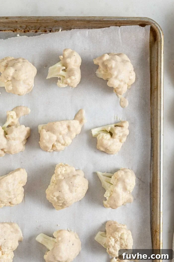 Tangy Buffalo Cauliflower Wraps 5 Raw cauliflower bites uniformly coated in batter, neatly arranged on a baking tray lined with parchment paper.