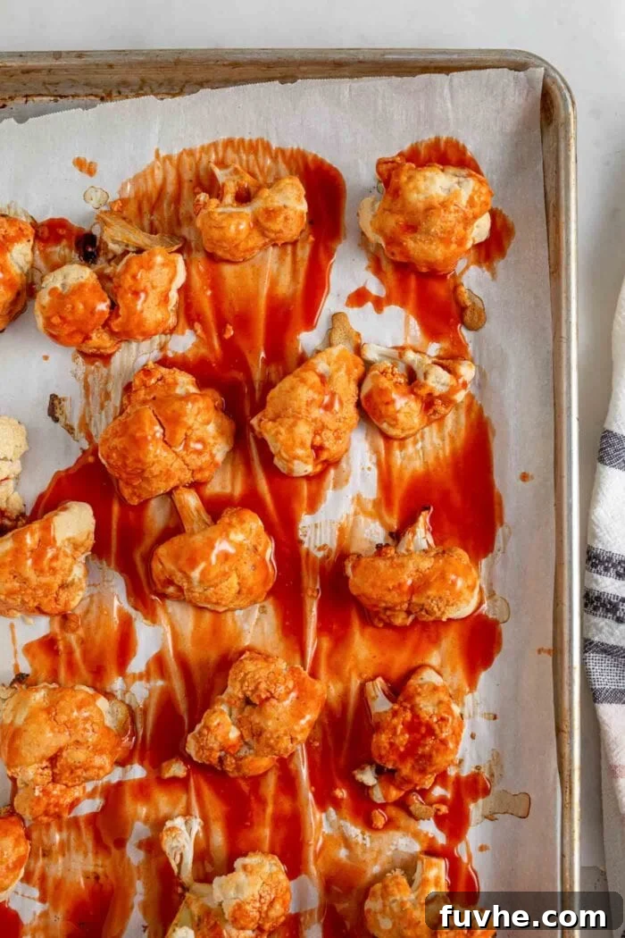 Tangy Buffalo Cauliflower Wraps 6 An overhead image of freshly baked buffalo cauliflower bites, glistening with sauce, spread out on a baking tray.