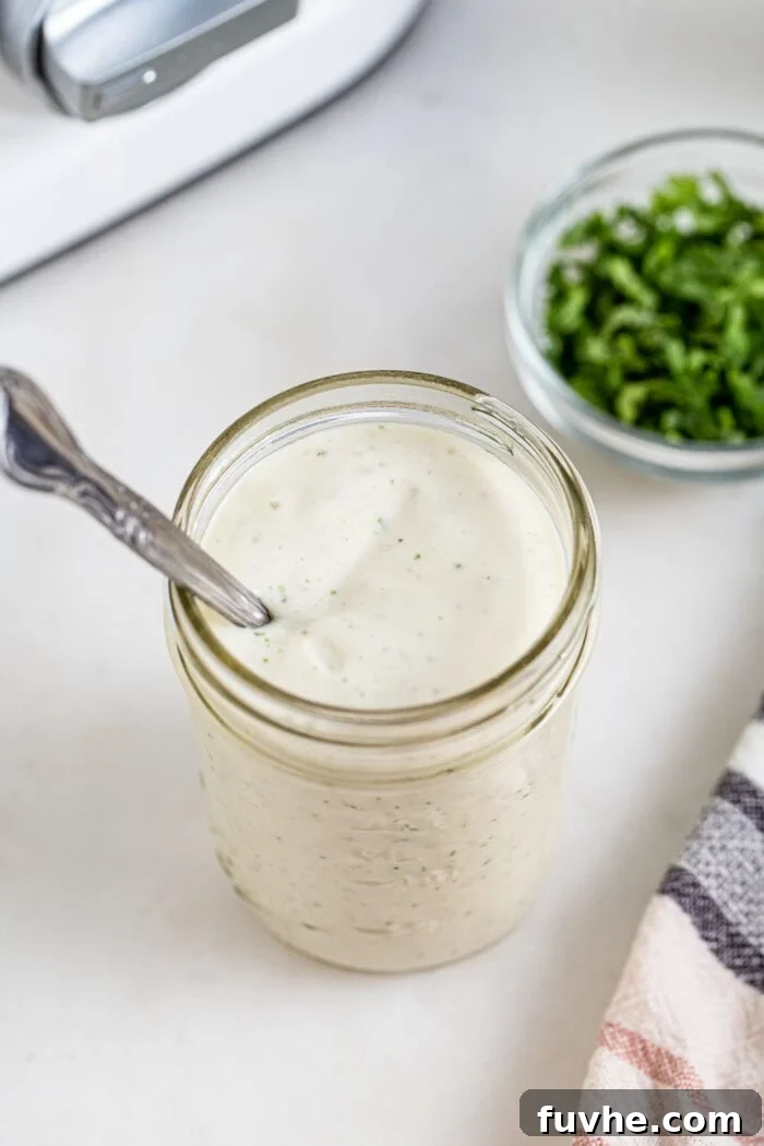Tangy Buffalo Cauliflower Wraps 7 A glass jar filled with creamy vegan ranch sauce, with a spoon resting inside, ready for serving.