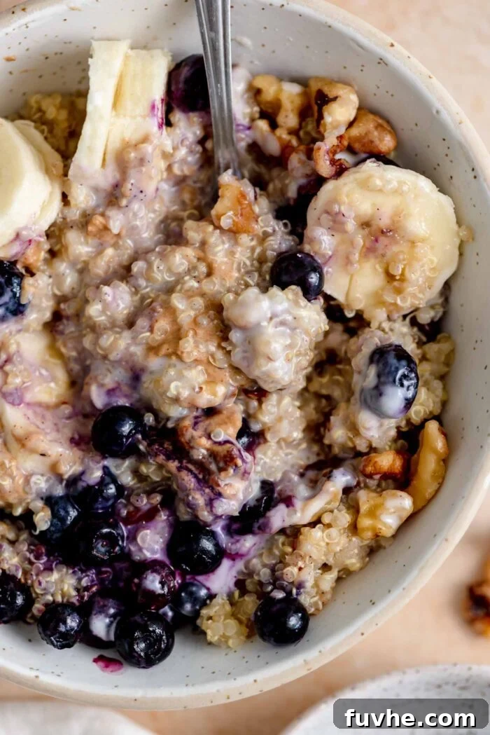 A beautifully presented bowl of breakfast quinoa, generously topped with fresh blueberries, sliced banana, creamy yogurt, crunchy walnuts, and a swirl of rich peanut butter, ready to be enjoyed.